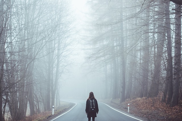 Girl standing in the middle of a foggy road, looking off in a different direction